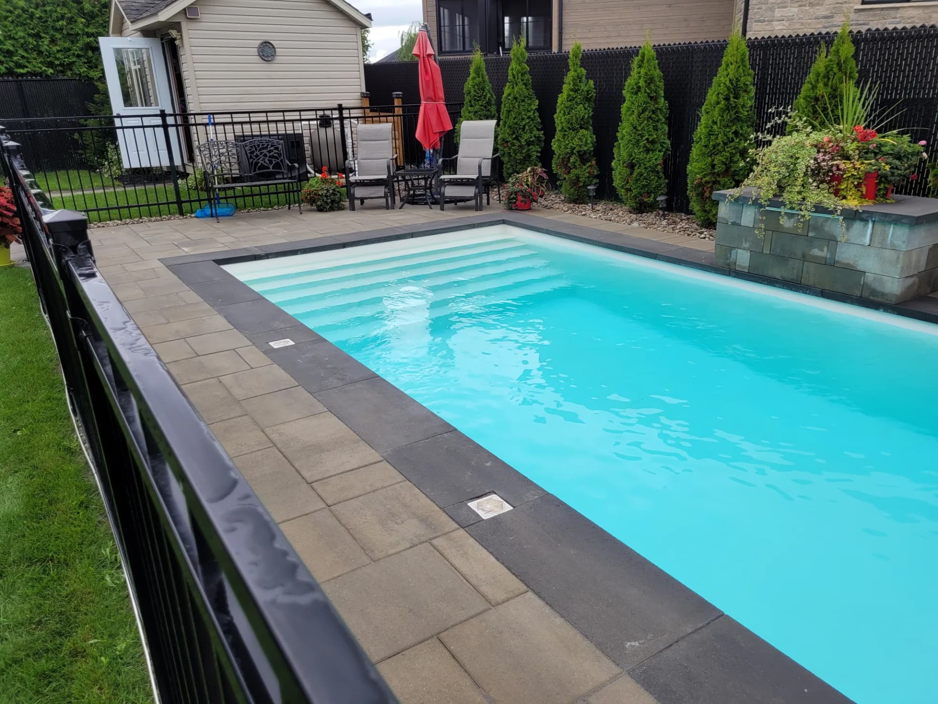 Piscine creusée avec contour en pavé, bac de plantation en pierre et cèdres matures