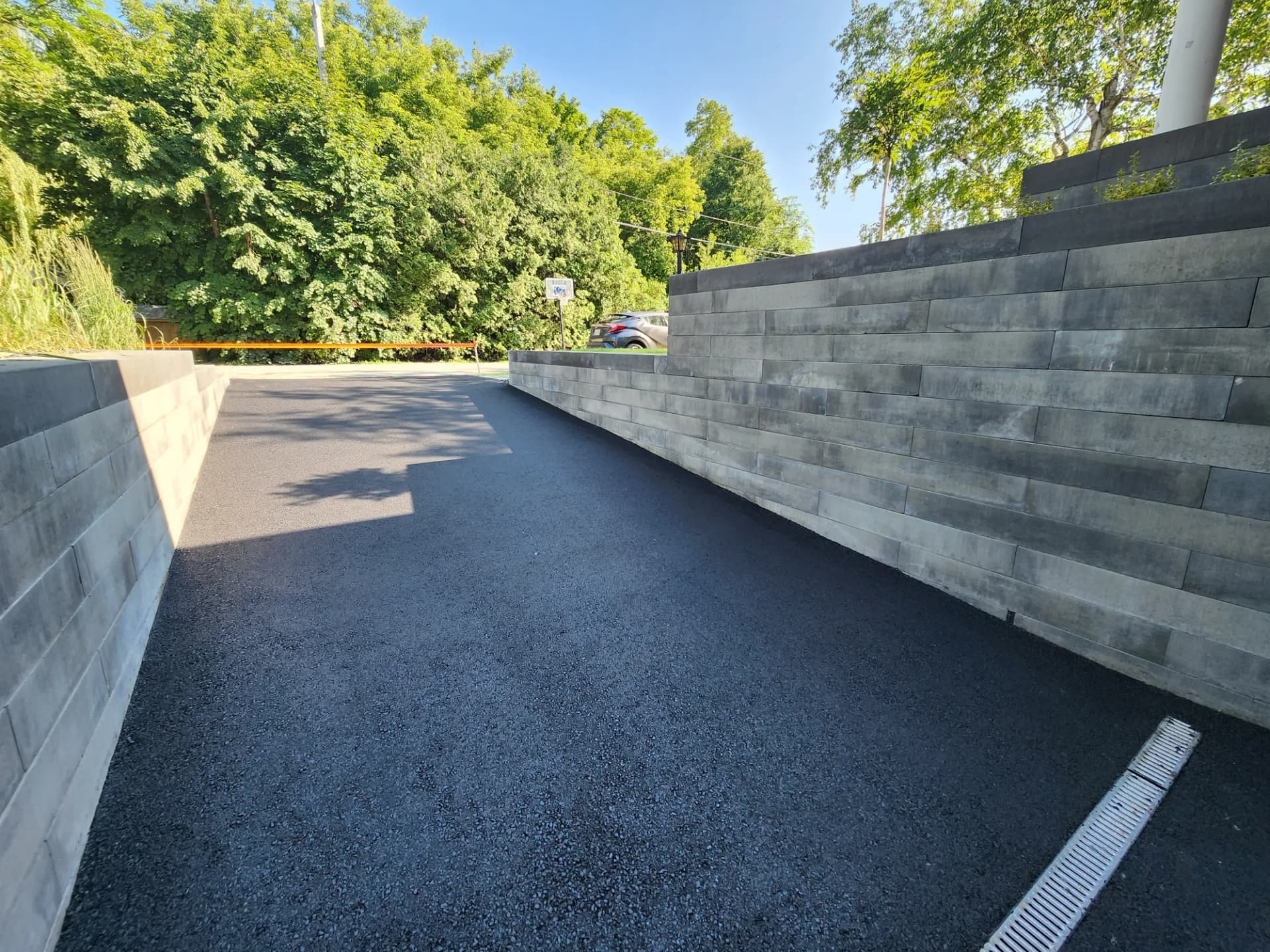 Long muret de soutènement en blocs architecturaux le long d'une entrée asphaltée