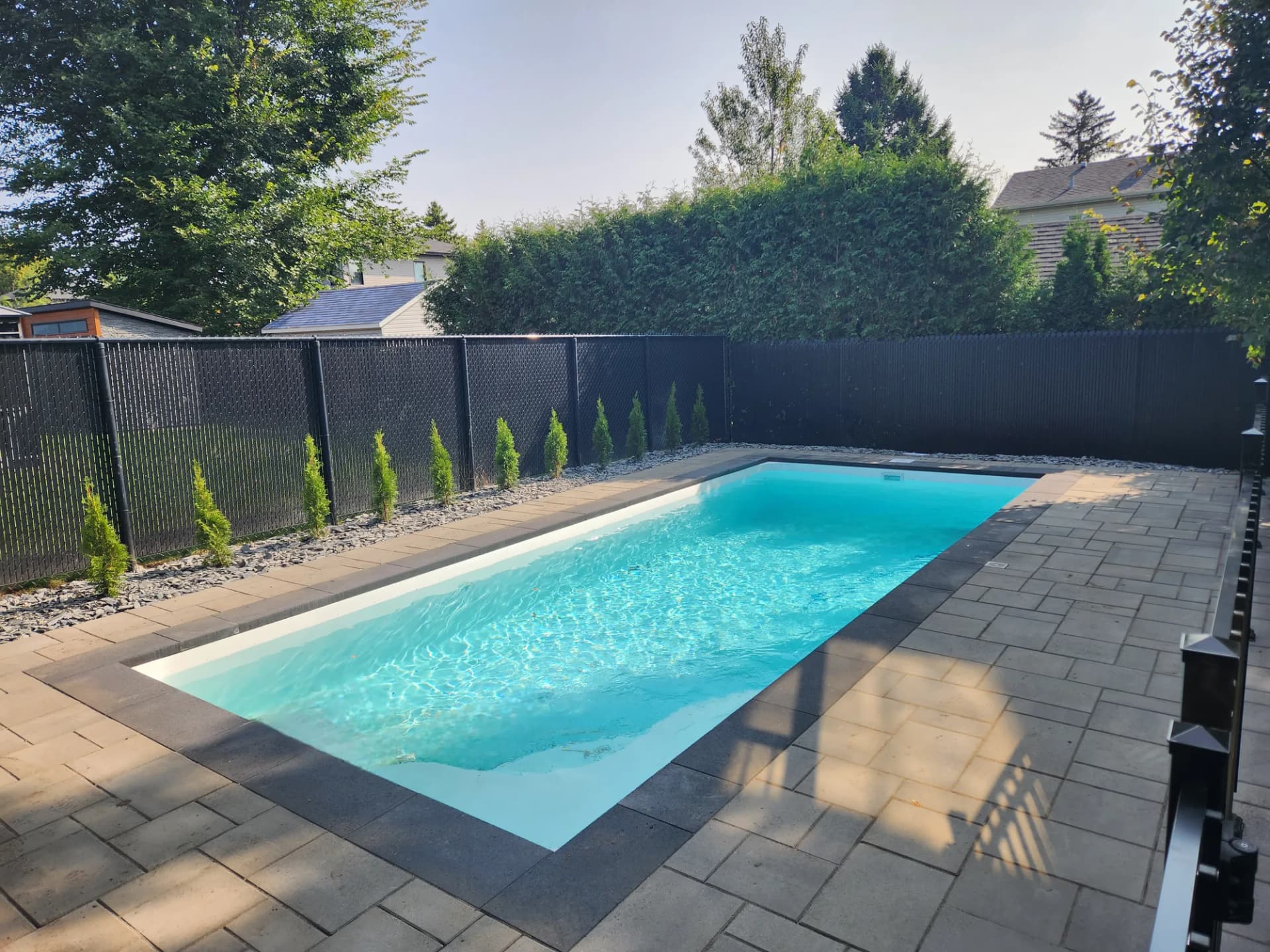 Piscine creusée avec contour en pavé, clôture noire et haie de cèdres sur la Rive-Sud