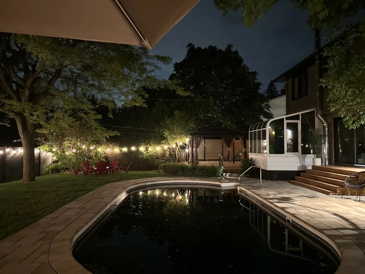Piscine creusée et terrasse en pavé éclairées le soir sous des guirlandes lumineuses