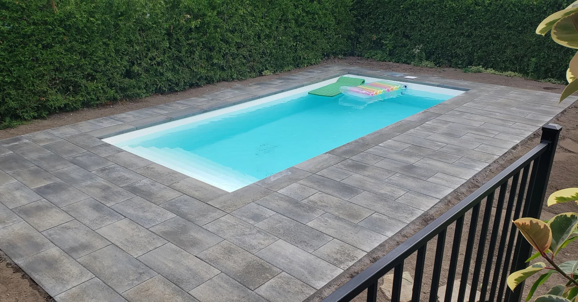 Piscine creusée entourée de pavé et d'une haie de cèdres, en soirée
