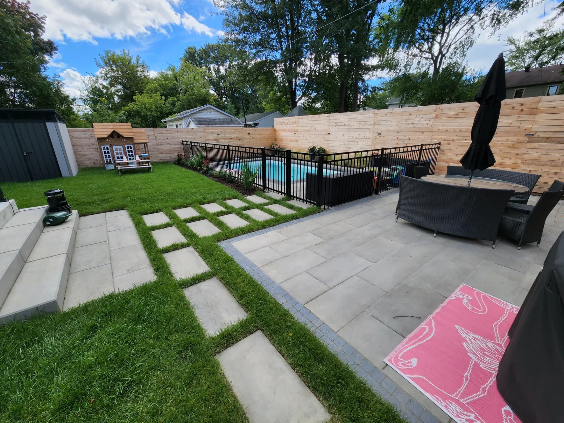 Terrasse en dalles, sentier de pas japonais et enceinte de piscine dans une cour aménagée