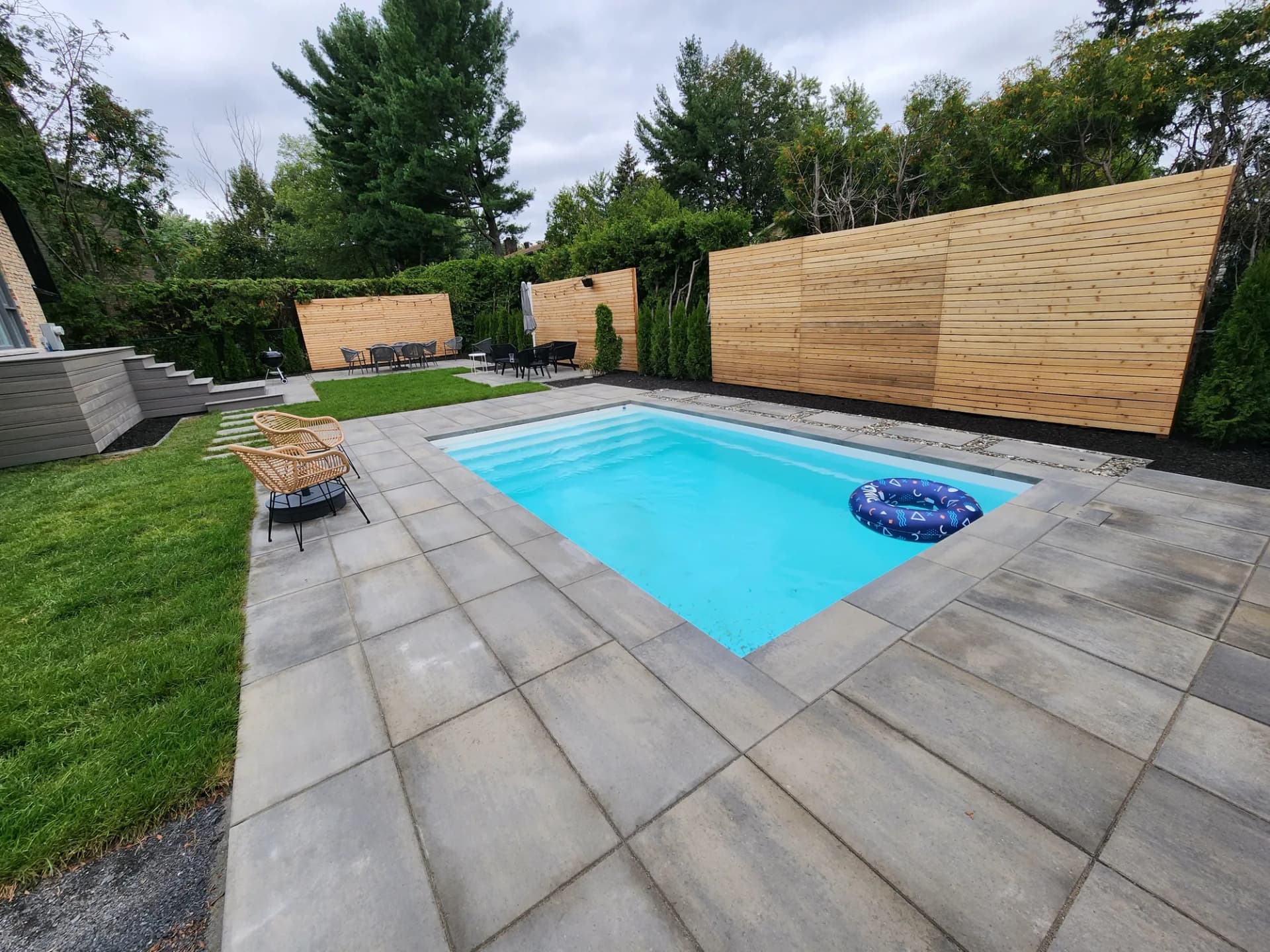 Contour de piscine en dalles de béton et cour arrière aménagée avec écrans d'intimité en cèdre